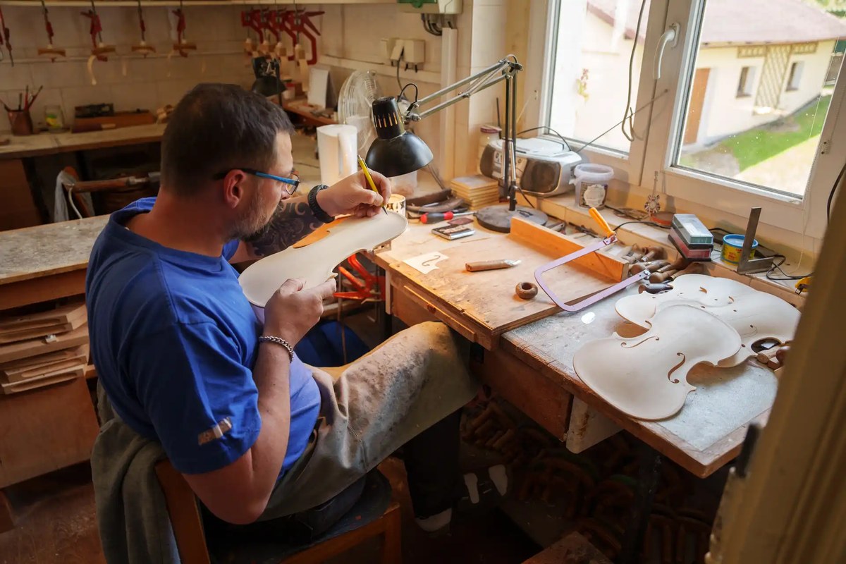 Houslař rýsuje na rezonanční desku houslí u pracovního stolu